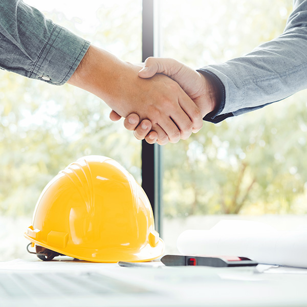 Two People shaking hands over a desk with construction material